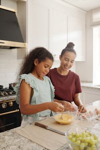 A joyful moment as a mother and daughter mix ingredients in the kitchen.