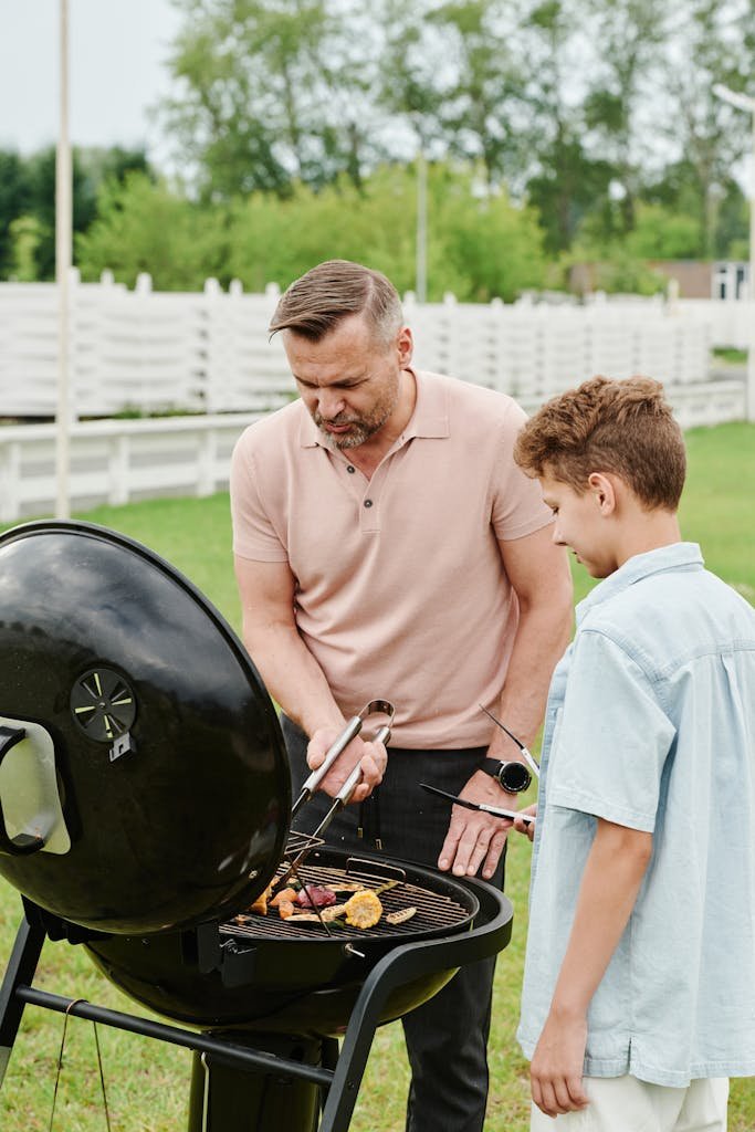 Father teaching son to grill on a summer day in the yard, fostering bonding and learning.