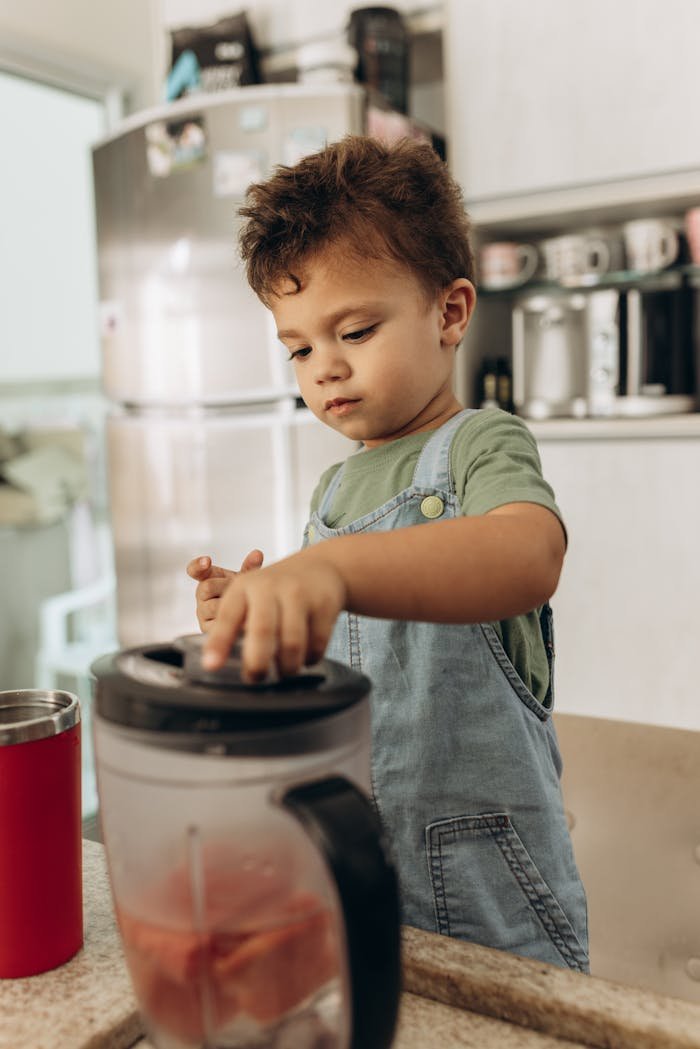 Young boy in overalls using a blender in the kitchen to make a smoothie.