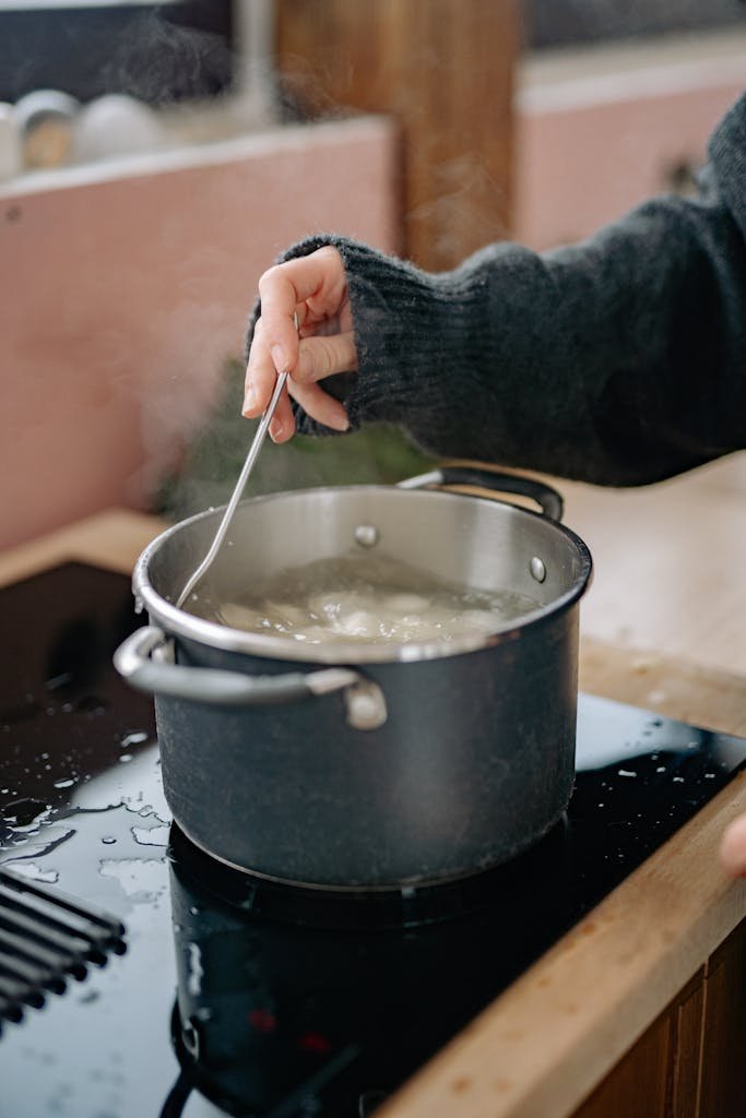 Hand stirring boiling dumplings in a pot on a stove, capturing home cooking.