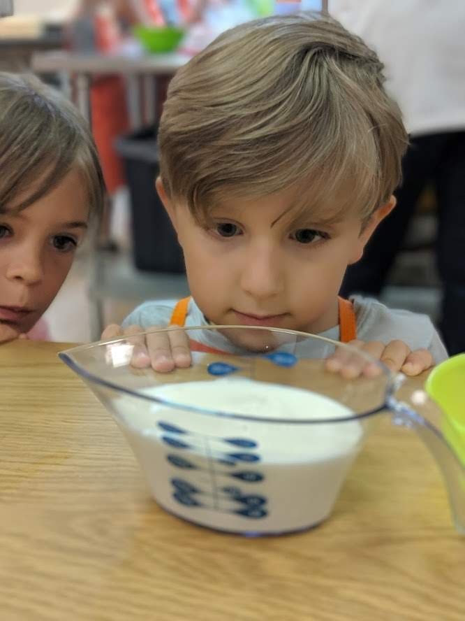 Students are looking at milk in a clear measuring cup to make sure the level of liquid met the exact mark and desired measurement.